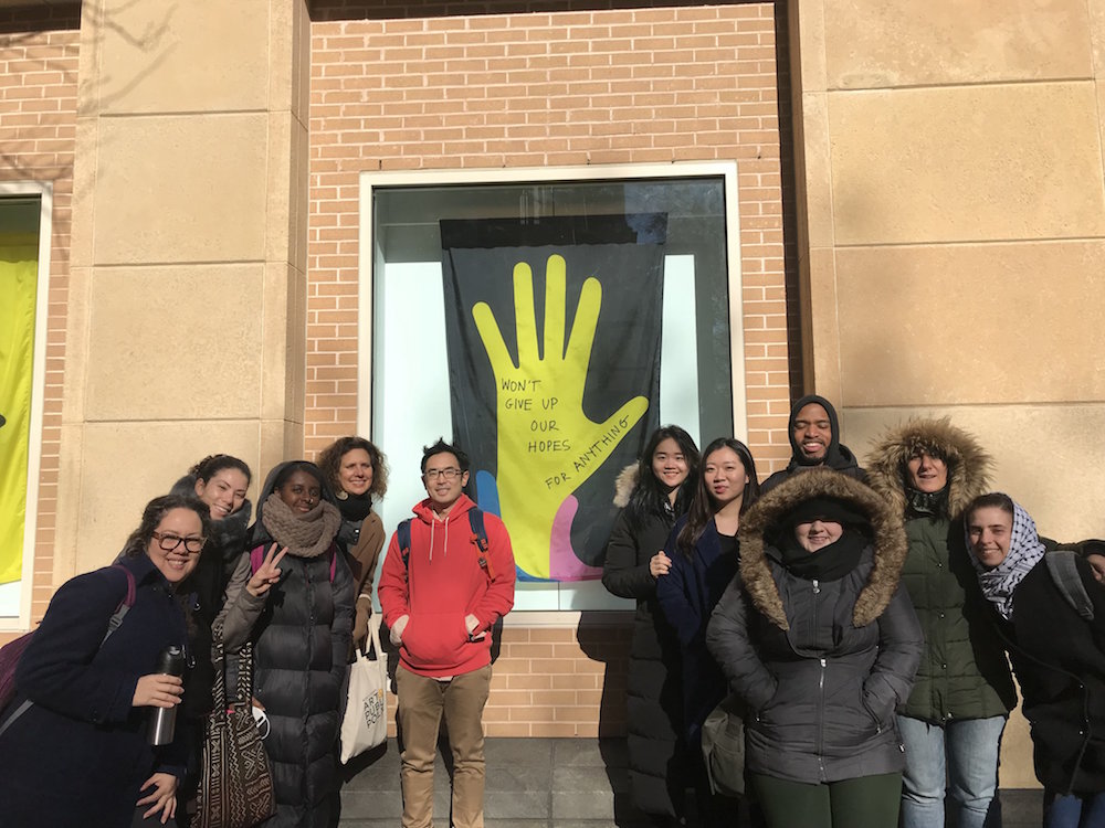 group stands in outdoors in front of window with yellow hand on black flag